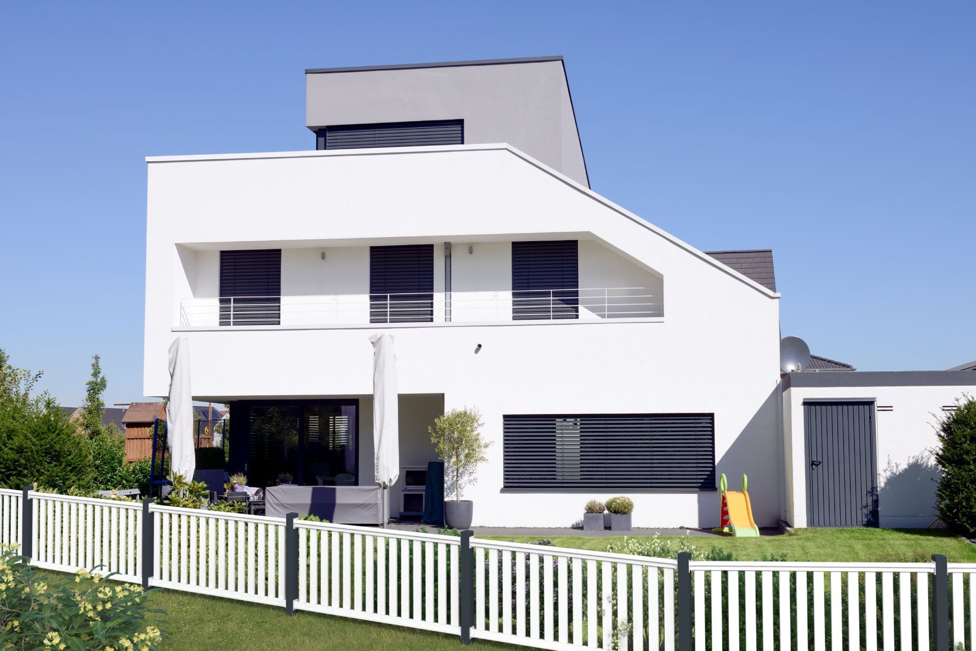 Railingzaun mit 82er Latte in weiß mit Pfosten in anthrazit - schräger Verlauf vor weißem Haus